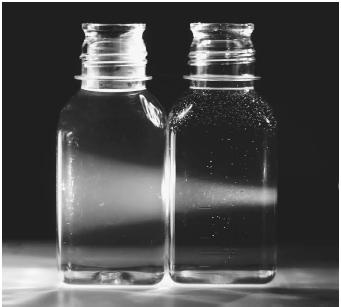 Light passing through a bottle containing sodium hydroxide (NaOH, left), and a bottle containing a colloidal mixture (right).