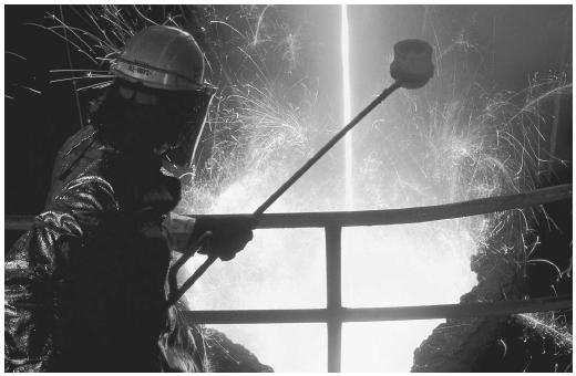 A steel worker is catching a sample of molten steel in a crucible during the manufacturing process.